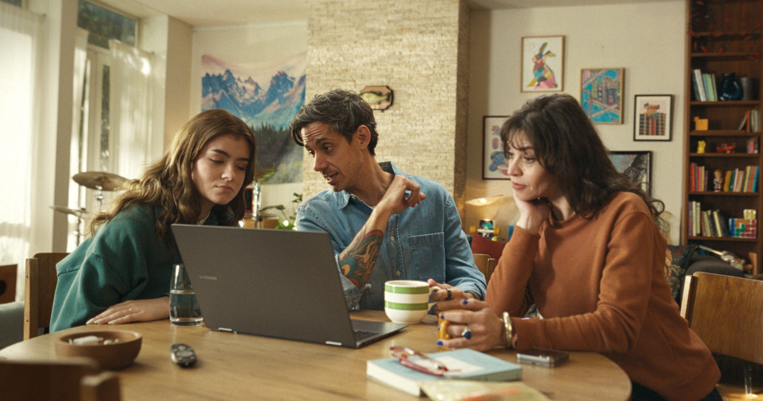 Tres personas sentadas en una mesa observando una notebook, en un ambiente hogareño cálido, representando el consumo de entretenimiento digital en familia
