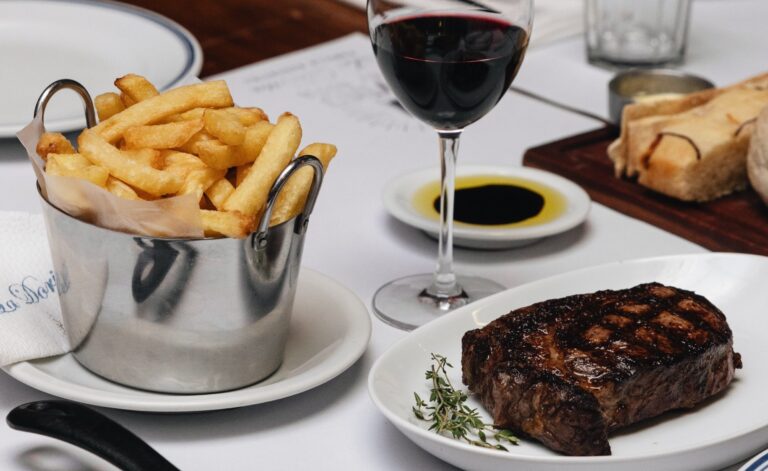 Plato de carne grillada con papas fritas, copa de vino tinto y pan artesanal, parte del menú completo de tres pasos que ofrece La Dorita