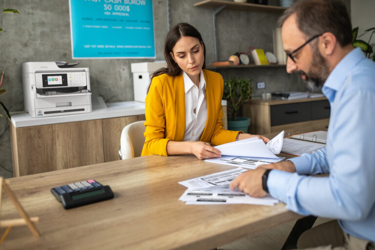 Dos personas revisan documentos impresos en una oficina moderna equipada con impresora Epson, simbolizando eficiencia y sustentabilidad en el entorno laboral