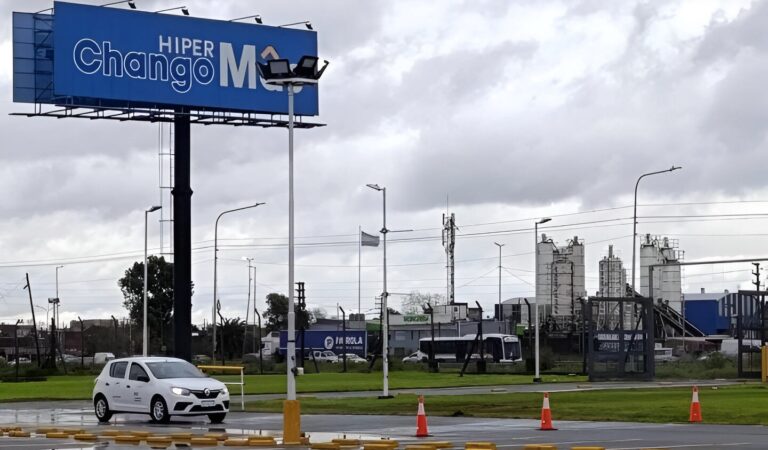 "Auto blanco en circuito de entrenamiento frente a un cartel de Hiper ChangoMás, durante una jornada del programa Conduciendo Oportunidades impulsado por Mujeres al Volante