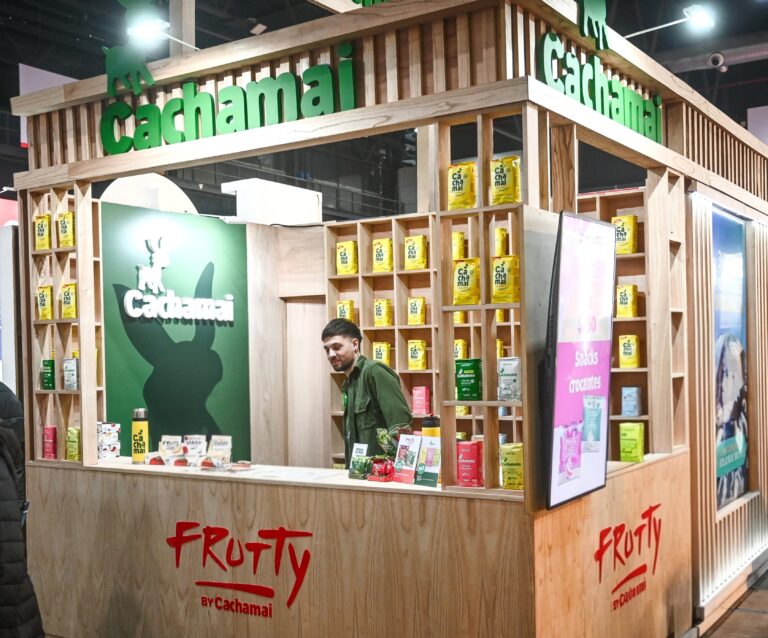 Stand de Cachamai en un evento, exhibiendo sus infusiones y productos Frutty en un diseño de madera con estanterías llenas de envases coloridos