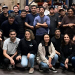 Grupo de empleados y empleadas posando juntos en un depósito, rodeados de estanterías con cajas y productos
