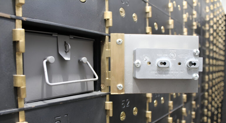 Vista cercana de una caja de seguridad privada abierta en una bóveda moderna, con cerradura de alta seguridad y múltiples compartimentos metálicos