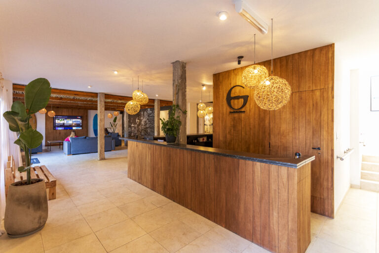 Vista de la recepción del complejo Las Golondrinas en Mar del Plata, con diseño cálido en madera, lámparas colgantes y sector de estar al fondo