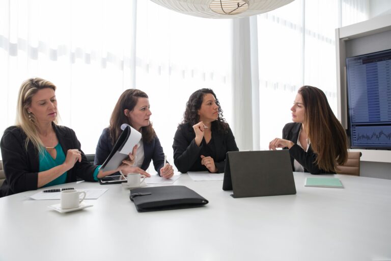 Cuatro mujeres ejecutivas argentinas dialogan durante una reunión de trabajo en una sala de reuniones con luz natural, documentos, tazas de café y una notebook sobre la mesa