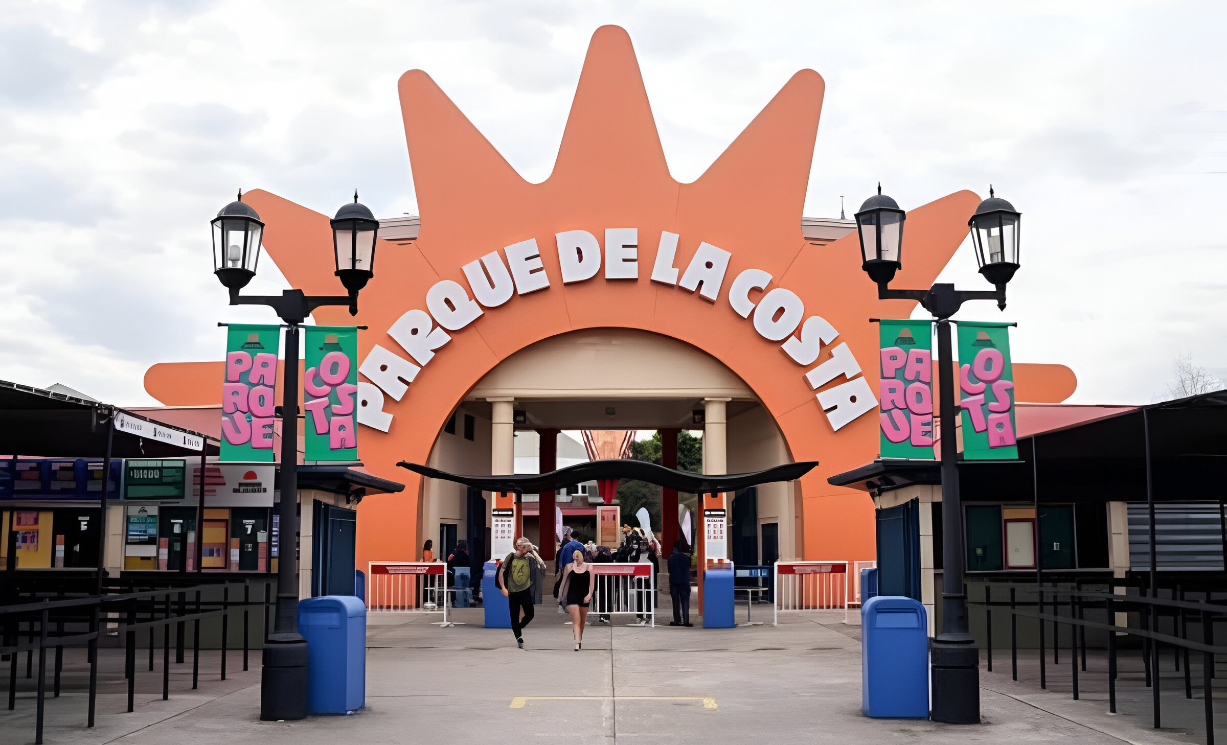 Vista frontal de la entrada del Parque de la Costa con su icónico cartel naranja y personas ingresando al parque