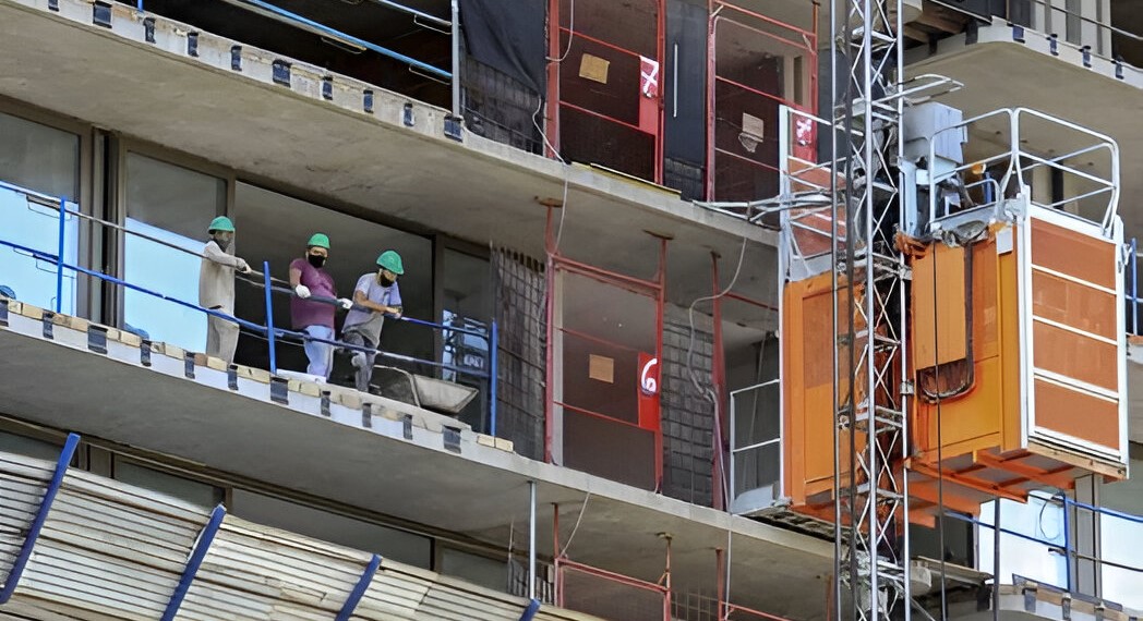 Obreros con casco en los pisos altos de un edificio en obra en Buenos Aires, junto a un montacargas de materiales en plena etapa de construcción desde el pozo