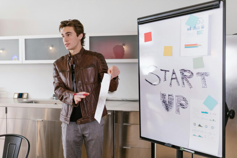 Joven emprendedor presentando ideas frente a una pizarra con la palabra “Startup” escrita a mano