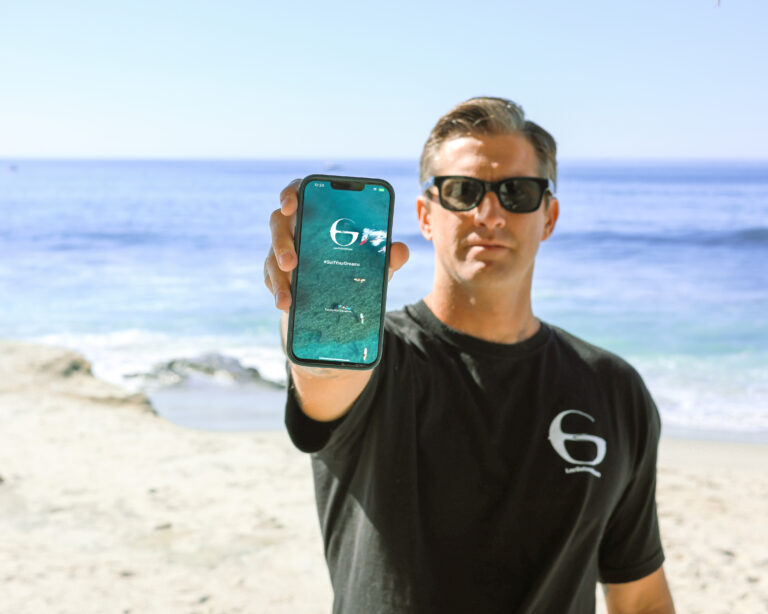 Gerónimo Usuna mostrando en su celular la nueva aplicación Las Golondrinas Mobile para viajeros, con el mar de fondo