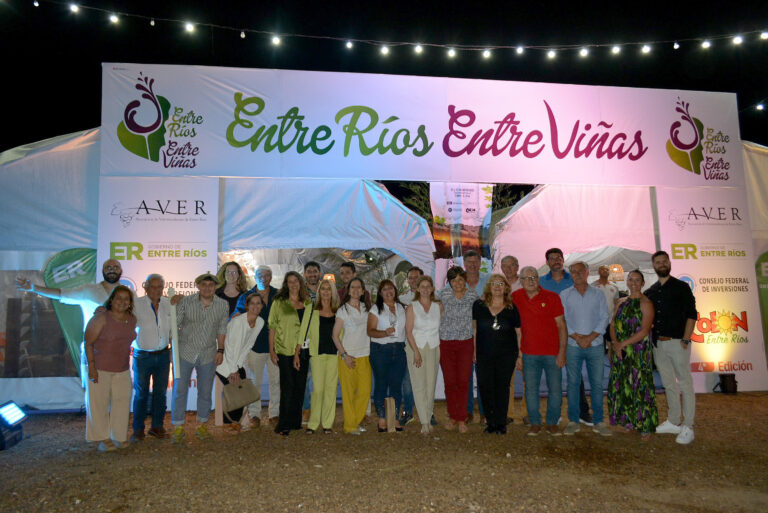 Grupo de personas posando frente al cartel de entrada de “Entre Ríos, Entre Viñas”, con iluminación nocturna y ambiente festivo