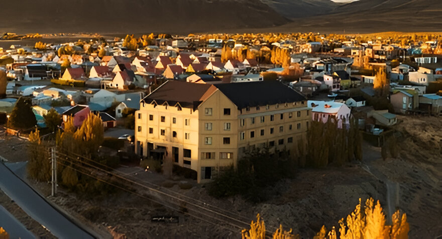 Imagen aérea del hotel Esplendor El Calafate rodeado de casas y árboles en tonos otoñales, con montañas al fondo