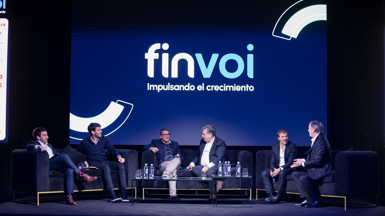 Disertantes conversando en el escenario durante el evento Finvoi, con el logo proyectado de fondo y ambiente profesional