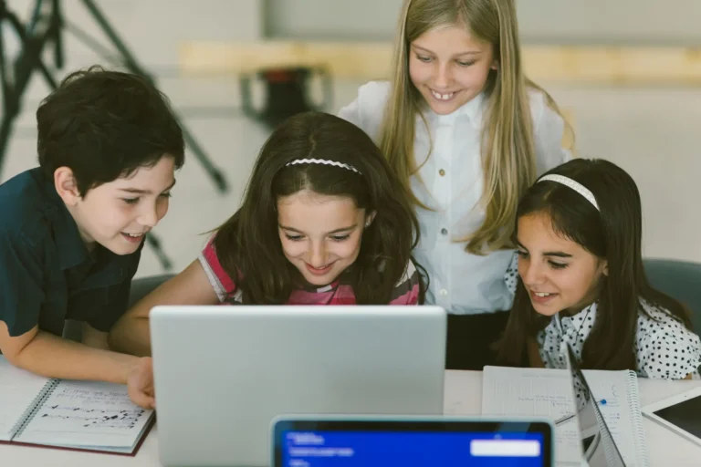 Grupo de chicos sonrientes usando una notebook para jugar o aprender en equipo