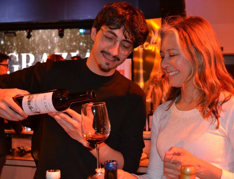 Un enólogo sirve vino en copa a una mujer sonriente durante EVISAN 2025 en San Juan, evento que celebra la identidad vitivinícola