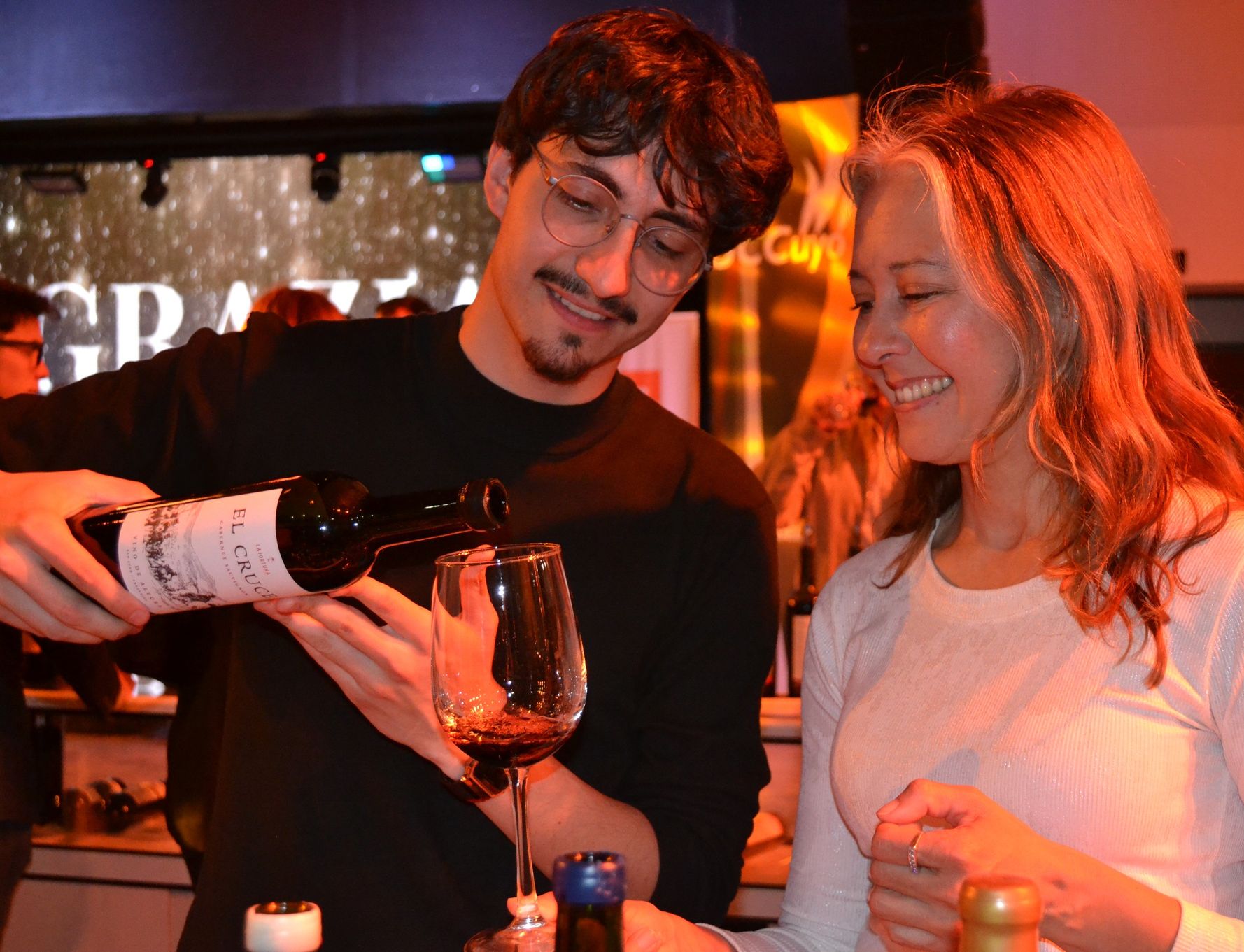 Un enólogo sirve vino en copa a una mujer sonriente durante EVISAN 2025 en San Juan, evento que celebra la identidad vitivinícola