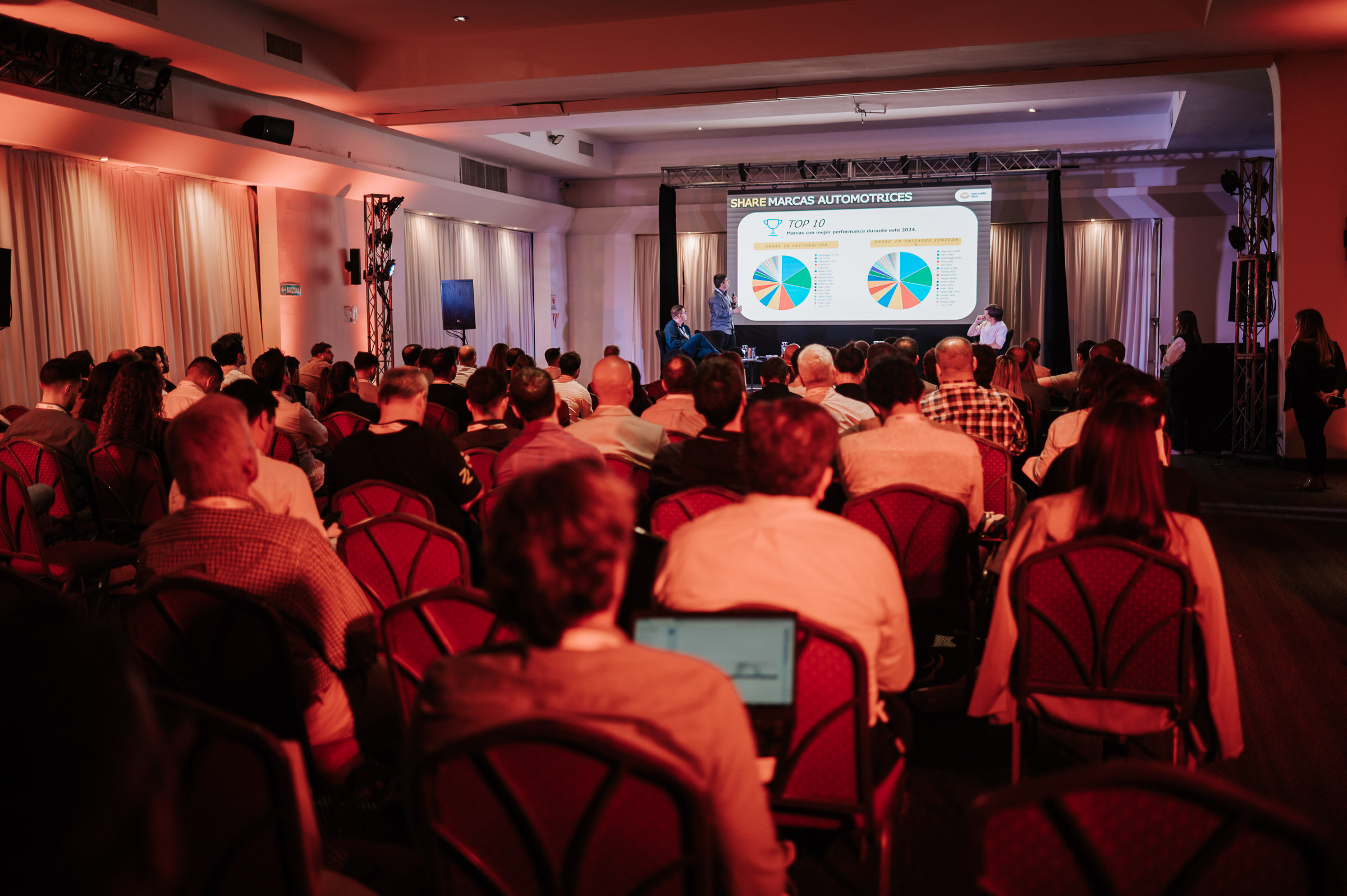 Sala llena en Auto.Tienda 2025 con asistentes observando una presentación sobre participación de mercado de marcas automotrices