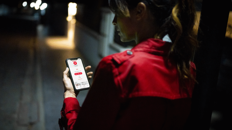 Mujer revisando su celular de noche en la calle, representando los riesgos del smishing y fraudes digitales