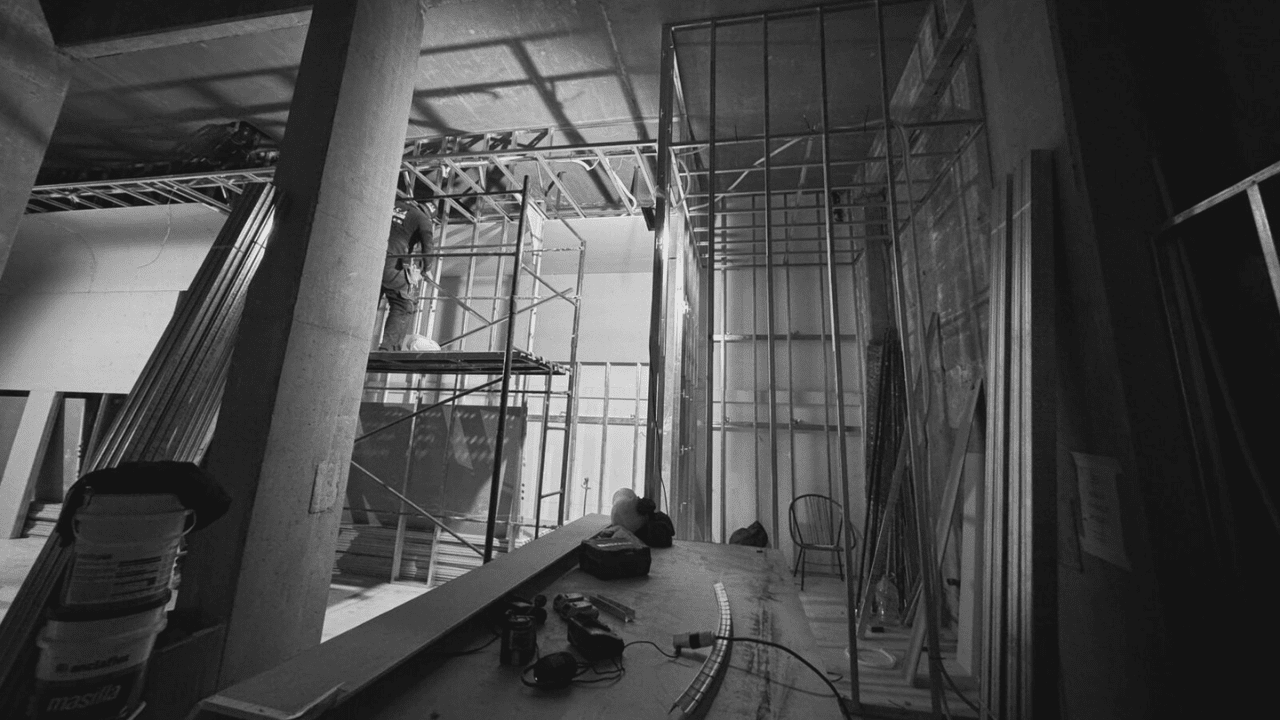 Vista en blanco y negro de la obra en construcción de Verona Disegni en Casa FOA, con estructuras metálicas y un trabajador sobre andamios