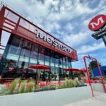 Fachada del nuevo local de Mostaza en Canning, con diseño moderno, terrazas al aire libre y el icónico logo rojo de la marca