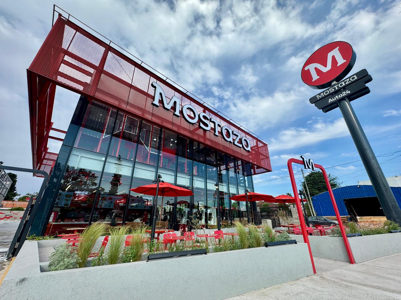 Fachada del nuevo local de Mostaza en Canning, con diseño moderno, terrazas al aire libre y el icónico logo rojo de la marca