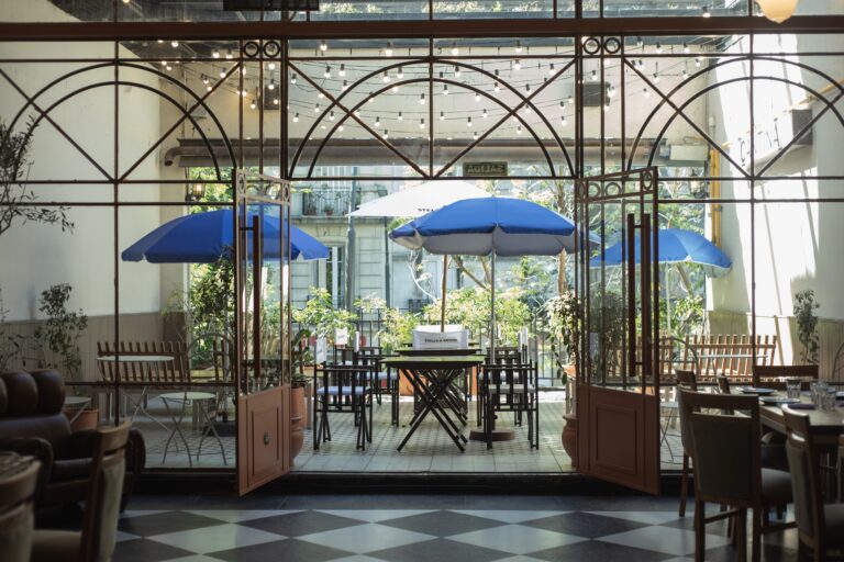 Terraza de Cantina Recoleta con mesas al aire libre, sombrillas azules y un ambiente luminoso que combina lo clásico y lo moderno