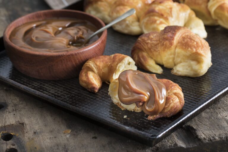 Medialuna con dulce de leche servida en bandeja junto a un cuenco de madera con más dulce