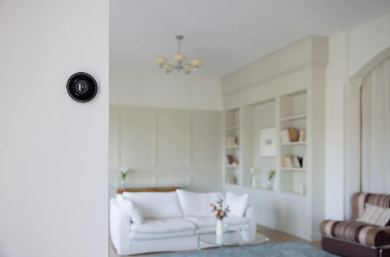 Cámara de seguridad instalada en la pared de un living luminoso con sillón blanco y estanterías