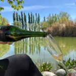 Persona sirviendo champagne Zamia Extra Brut junto a un lago rodeado de viñedos en Mendoza