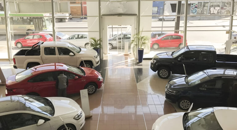 Vista interior de un concesionario con autos usados exhibidos y clientes evaluando vehículos en venta
