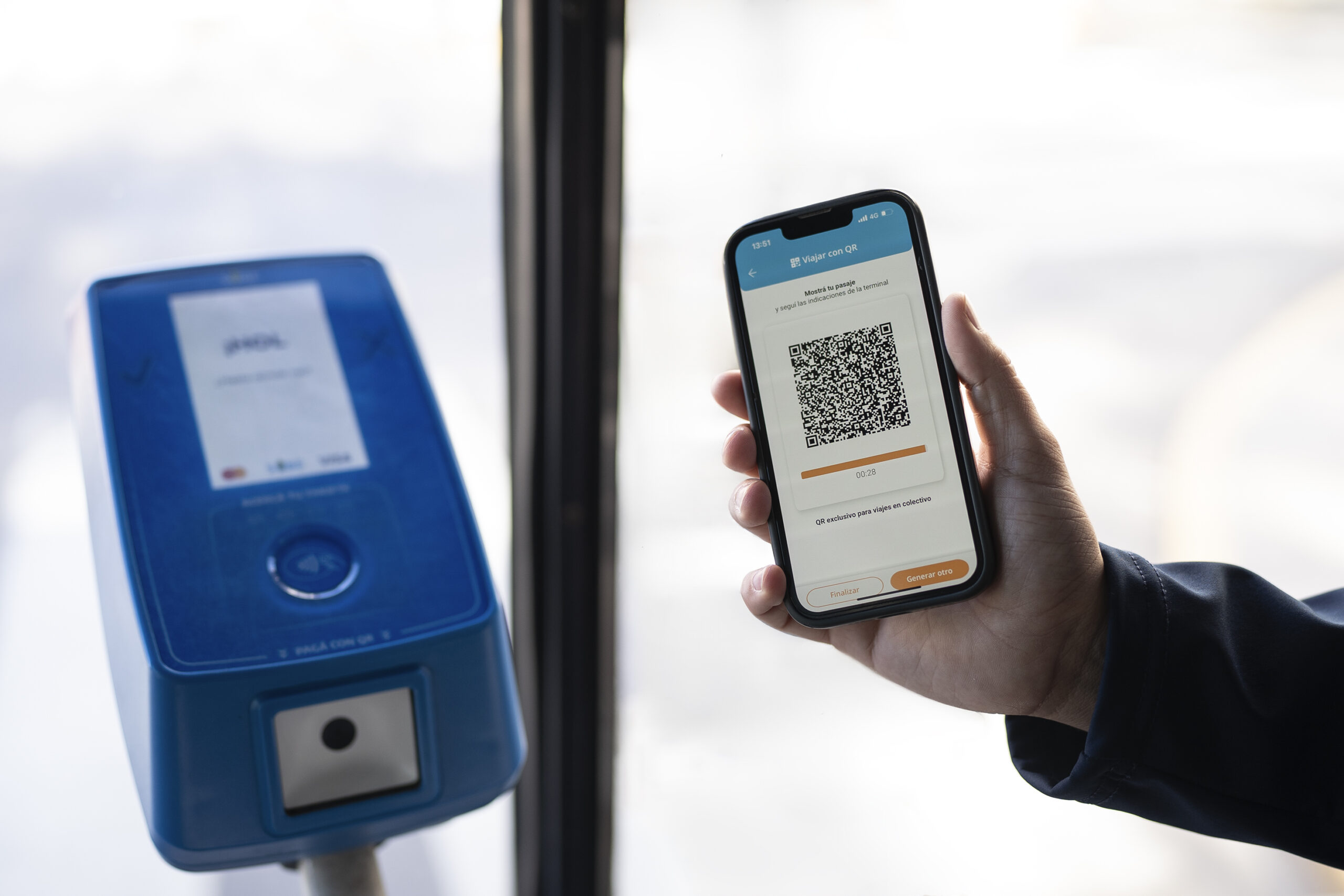 Persona mostrando un código QR en el celular para pagar el viaje en colectivo frente a una validadora azul