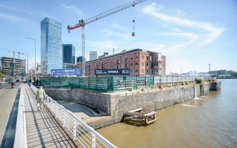Obras del proyecto Portal Buquebus en Puerto Madero con grúa y edificio de ladrillos junto al río y carteles de CRIBA