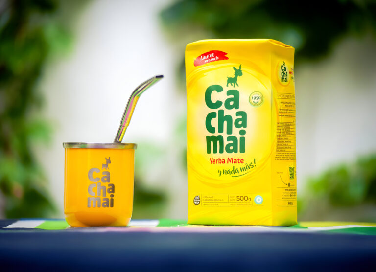 Mate de calabaza con bombilla junto a yerba en un cuenco y un paquete amarillo, sobre una mesa de madera en ambiente cálido