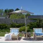 Reposeras de madera con almohadones y sombrilla junto a una piscina en un jardín