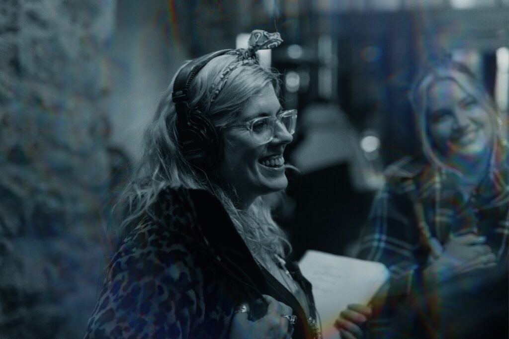 Mujer con auriculares y libreta sonriendo durante una producción audiovisual, representando el trabajo creativo en equipo