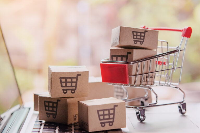 Carrito de compras en miniatura y cajas pequeñas con íconos de e-commerce sobre un escritorio, simbolizando el aumento de ventas online
