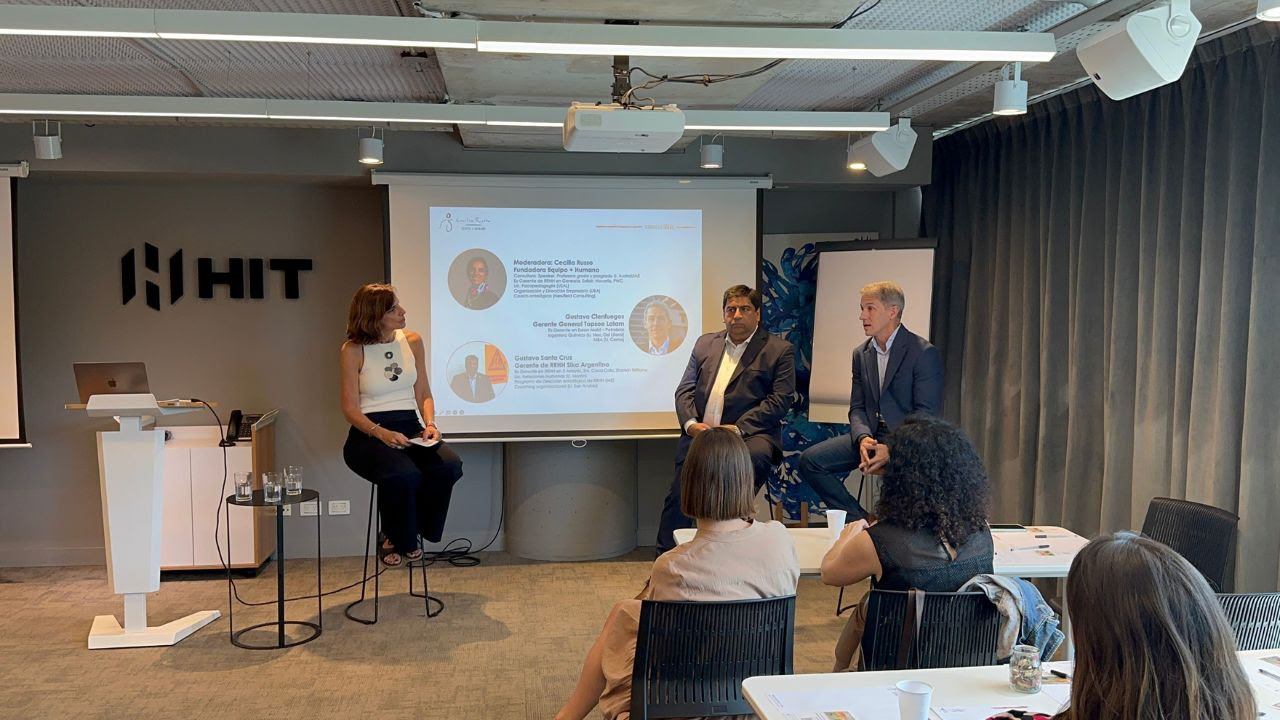 Panel de líderes empresariales en un encuentro profesional, con una moderadora y dos expositores dialogando ante un público en un espacio corporativo