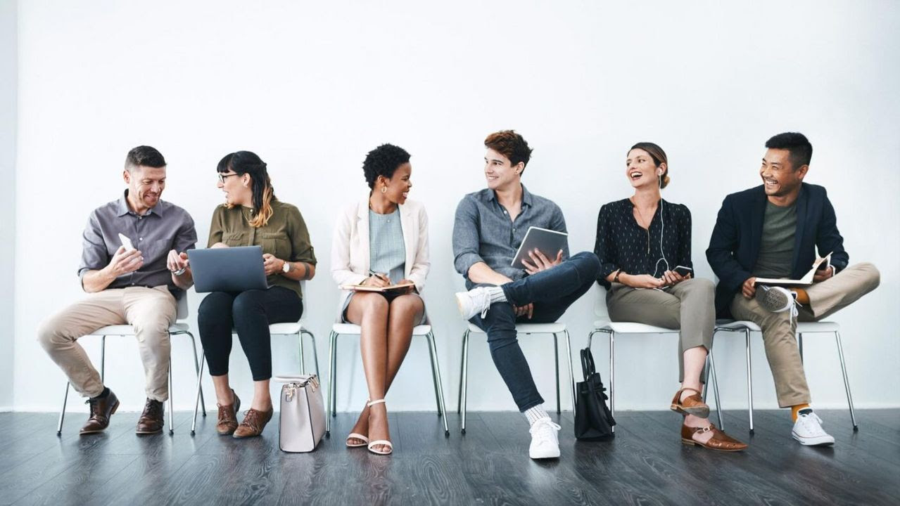 Grupo de personas sentadas en una sala de espera conversando y trabajando con dispositivos, representando la movilidad laboral y los nuevos formatos de carrera profesional