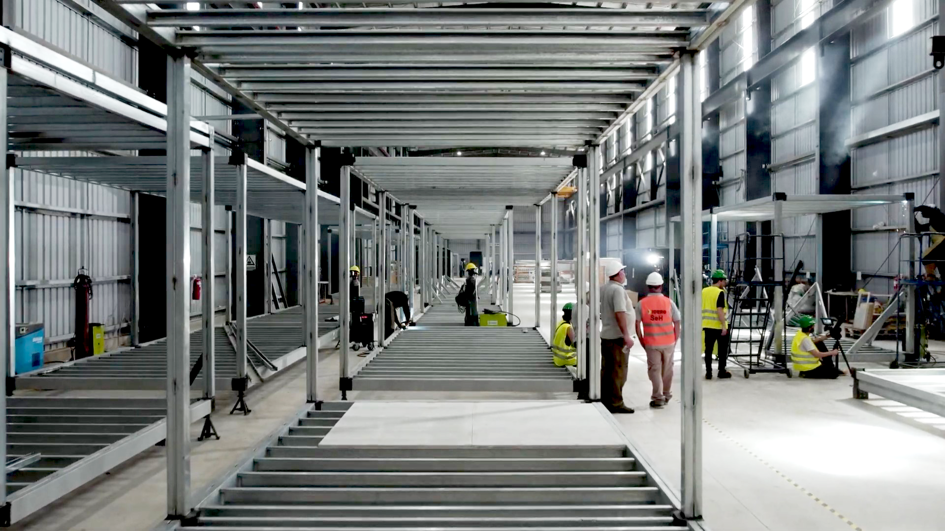 Interior de obrador industrial en Vaca Muerta con estructuras metálicas en montaje y trabajadores argentinos con cascos y chalecos de seguridad durante una obra energética