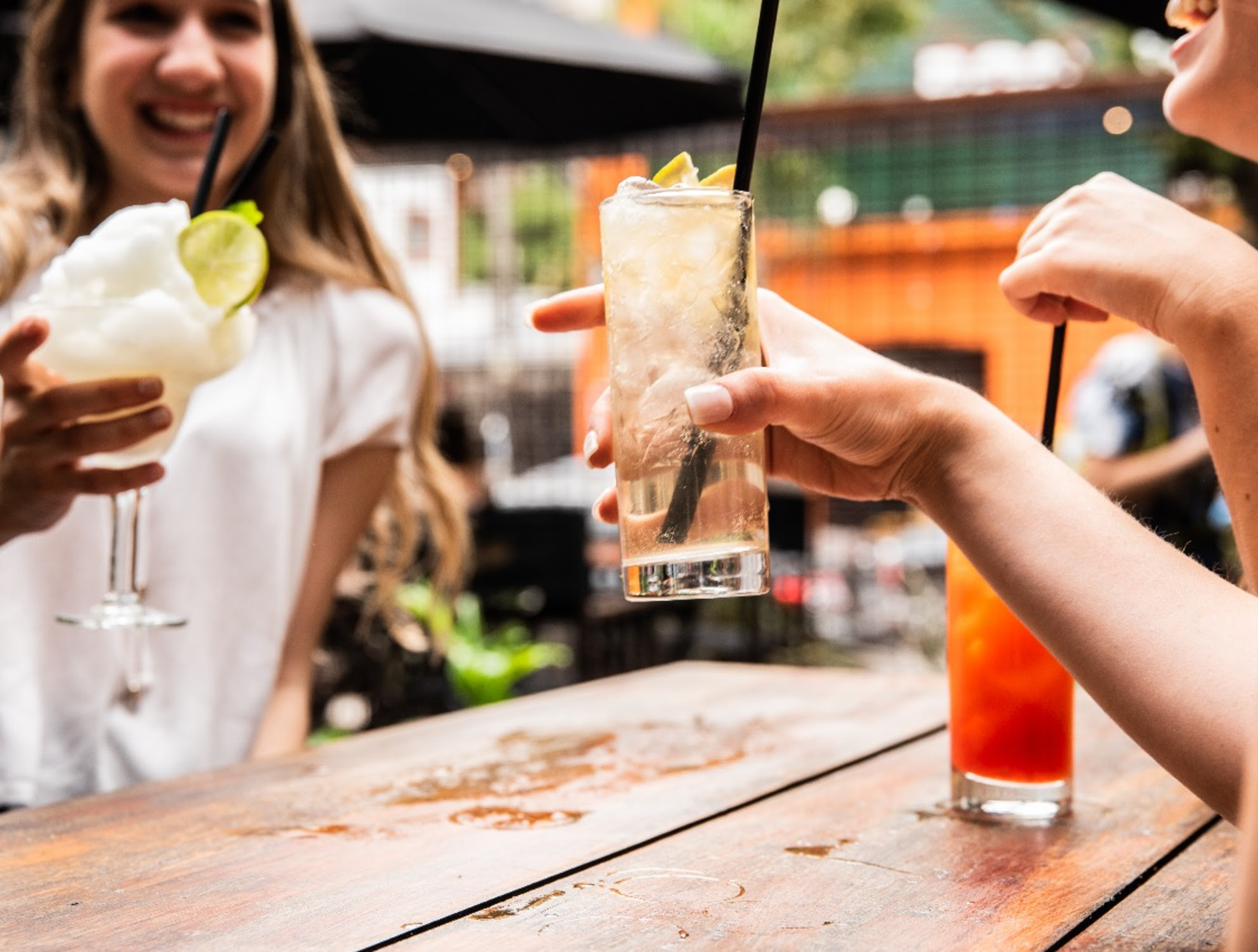 Personas brindando con cócteles y tragos en una mesa al aire libre, en un bar porteño, durante una promoción especial para compartir en Malcriado