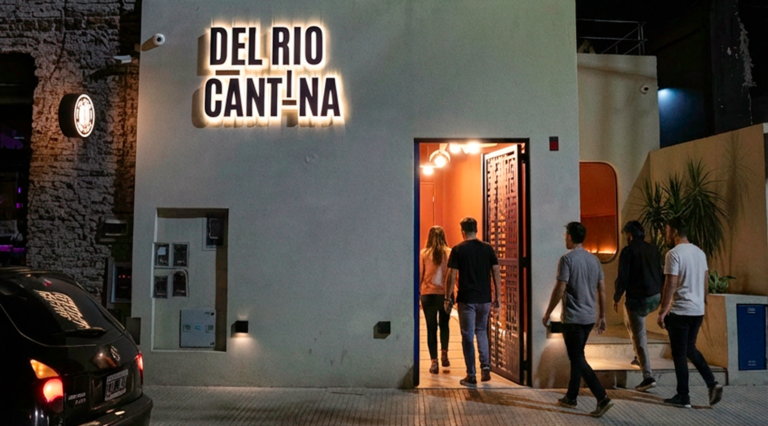 Fachada iluminada de Del Río Cantina en Buenos Aires con clientes ingresando al restaurante tras la renovación de su carta con platos para compartir