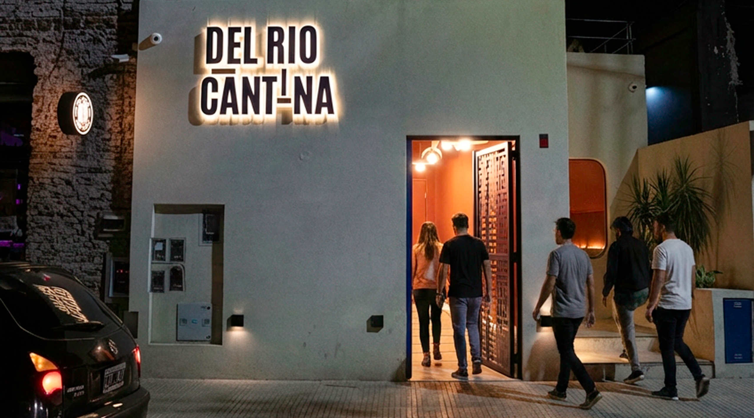 Fachada iluminada de Del Río Cantina en Buenos Aires con clientes ingresando al restaurante tras la renovación de su carta con platos para compartir