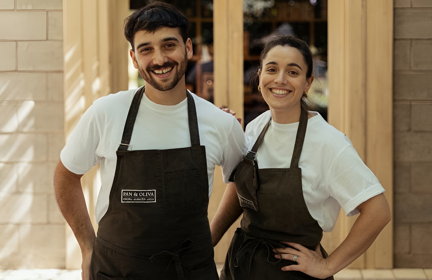 Mecha Ferraro y Lucio Zibecchi sonríen con delantales de Pan y Oliva frente a la entrada del restaurante en Mendoza