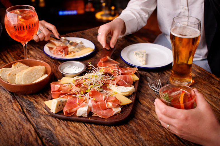 Picada de quesos y fiambres con cerveza y cócteles en una mesa de bar estilo after office