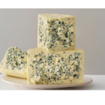 Bloques de queso azul sobre plato blanco con vetas características y textura cremosa en primer plano sobre fondo neutro