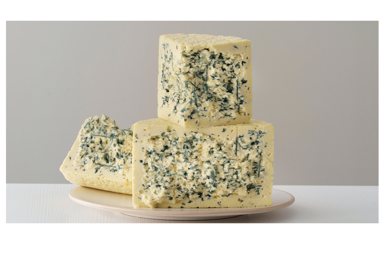 Bloques de queso azul sobre plato blanco con vetas características y textura cremosa en primer plano sobre fondo neutro