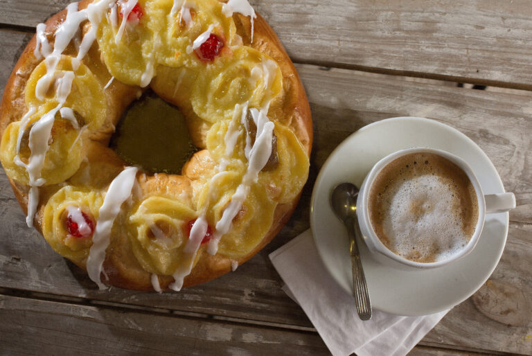 Rosca de Pascua artesanal con crema pastelera y frutas acompañada de café sobre mesa de madera