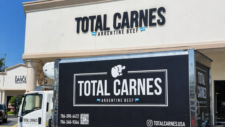 Camión de Total Carnes frente a su local en Estados Unidos con branding de carne argentina y fachada del establecimiento