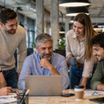Equipo de trabajo con personas de distintas edades colaborando frente a una computadora en una oficina moderna