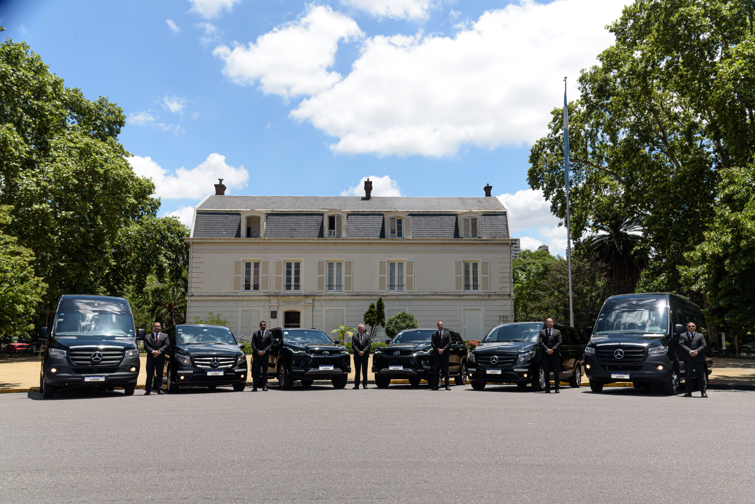 Flota de vehículos ejecutivos con choferes uniformados frente a un edificio institucional en el marco de servicios de logística para eventos