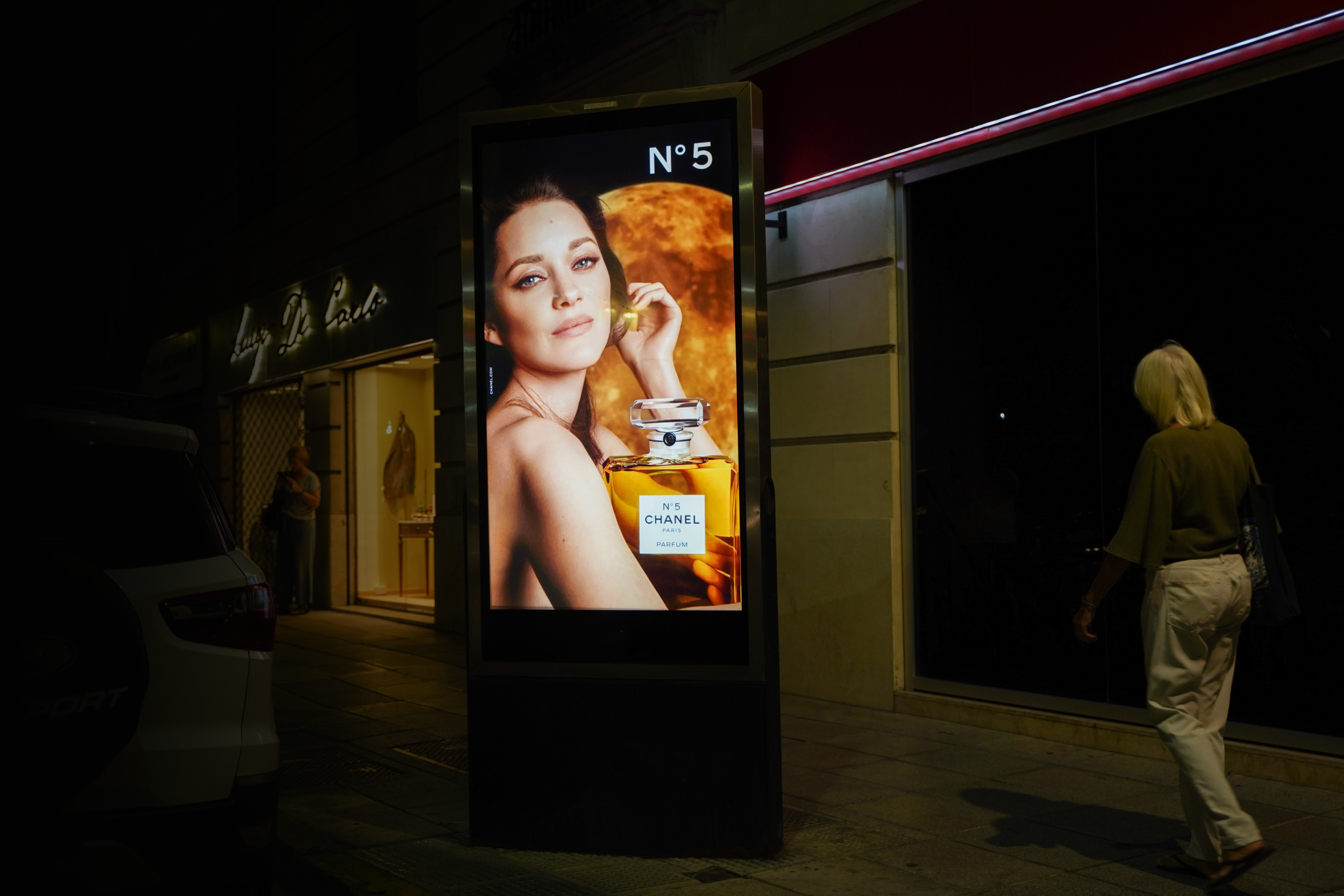 Pantalla publicitaria digital en la vía pública durante la noche con anuncio iluminado mientras una persona camina por la vereda urbana